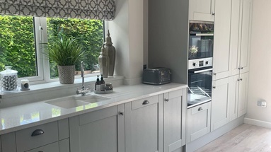 Grey single wall kitchen idea with shaker cupboards, silver cup handles, a white worktop and inset sink, and grey oak floors.