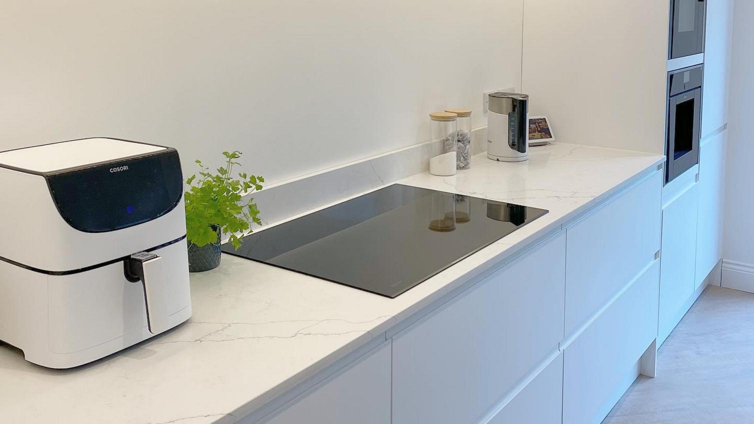 White single wall kitchen idea with integrated handle cupboards, a white marble effect worktop and integrated appliances.