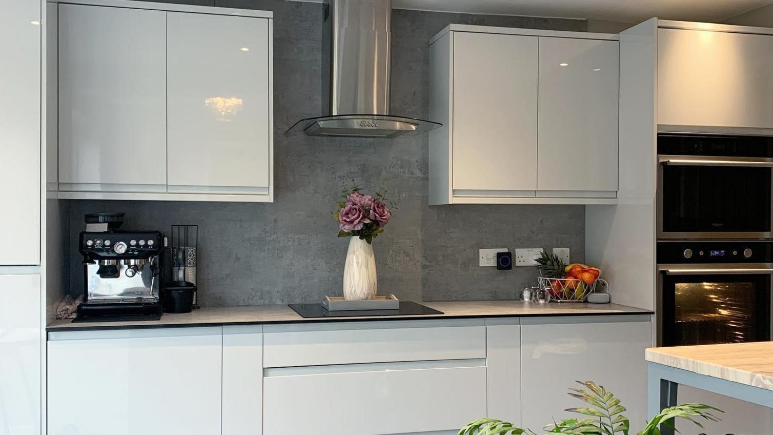 White single wall kitchen idea with integrated handle cupboards, a grey worktop, induction hob and integrated appliances.