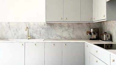 Grey L-shaped kitchen idea using slab cupboard doors, marble-effect backboards, and brass knob handles for a luxe look.