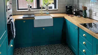 Turquoise kitchen design in a u-shaped layout with monochrome floor tiles, a Belfast sink, wooden counters, and white tiles.