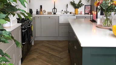 Two-tone open-plan kitchen idea with a dark green island and light-grey wall units, green plants, and white worktops.