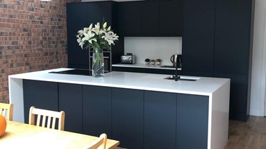 Navy slab kitchen design with an island, a white wraparound worktop, and medium oak panelled flooring.