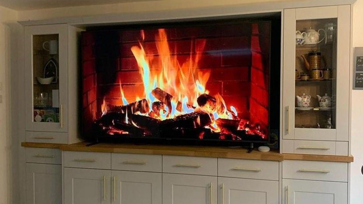Simple living room idea using brushed brass bar handles on grey shaker cupboard doors. Has glass wall units and oak worktops.