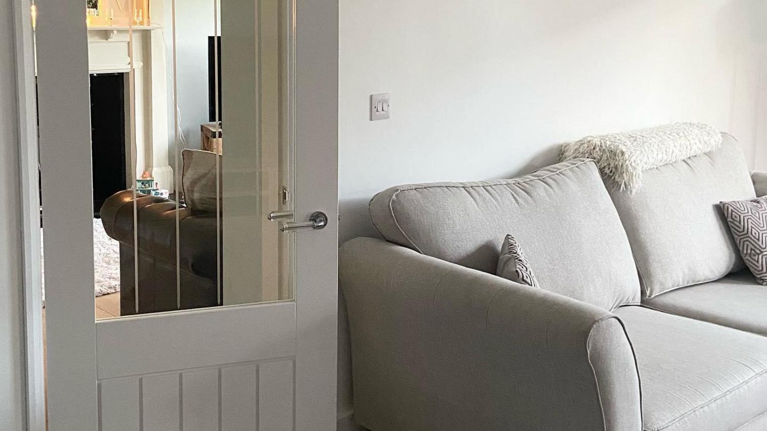 A simple living room idea featuring a glazed door for a bright look. Includes white walls, grey carpets, and a cream sofa.