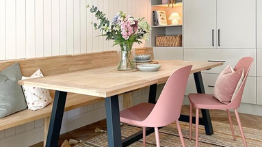 Scandi dining room idea with light grey slab doors, black handles, a custom oak bench, an oak table and pink chairs.
