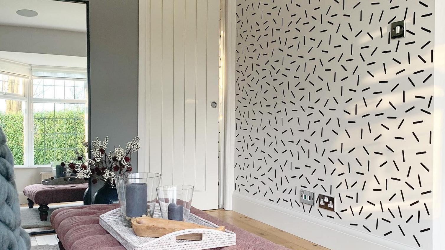 White panelled pocket door in a living room design, with a pink ottoman, wood flooring, and a monochrome pattern wallpaper.