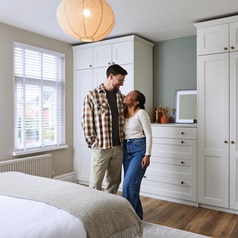 Jade and James standing in their new Bridgemere bedroom. It has oak vinyl flooring, tall wardrobes and matching drawer units