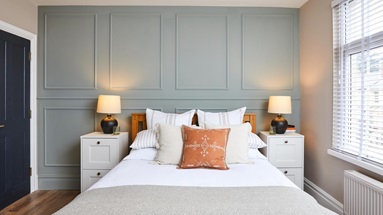 A feature wall above a bed, made using wall mouldings and painted in a muted great colour. Adjacent is a navy doorway.
