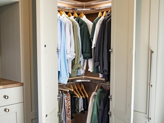 A Halesworth shaker sage green corner wardrobe, with hanging rails and strip lighting inside.