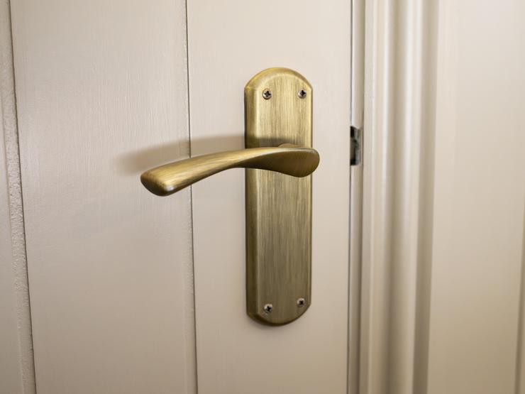 A brass Fuller and Forge door handle, on a tongue-and-groove door. The door is painted in a cream colour.
