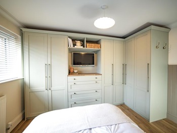 The finished bedroom makeover, with Halesworth sage green drawers and cabinets, wall panelling, and oak-style flooring.
