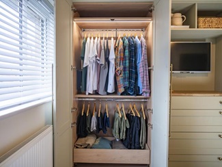 A Halesworth bedroom wardrobe, open to show clothes hanging rails inside. There is also drawer storage and LED strip lights.