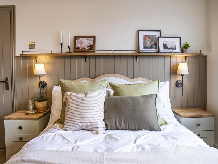 Painted wall panelling sits behind a large bed, with sage green bedside tables on either side.