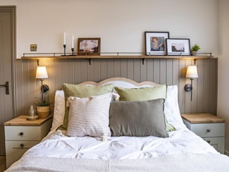 Painted wall panelling sits behind a large bed, with sage green bedside tables on either side.