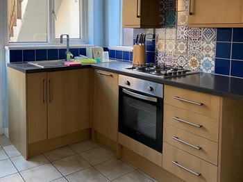 Oak l--shaped kitchen with black worktop, silver bar handles and gas hob