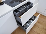 A compact white kitchen with two pan drawers and cutlery tray fitted beneath a black induction hob.