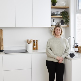 Women leaning against the sink in a white handleless kitchen with super matt cupboard doors and wooden shelving.