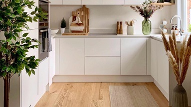 A small white kitchen makeover using matt handleless cupboards, white quartz worktops and wood flooring.