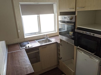 Old-fashioned kitchen with missing cabinets, old dark wood worktops and dated appliances.
