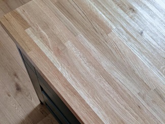 Birds eye view of a grained wood worktop, with matching oak flooring and dark green shaker cupboards.