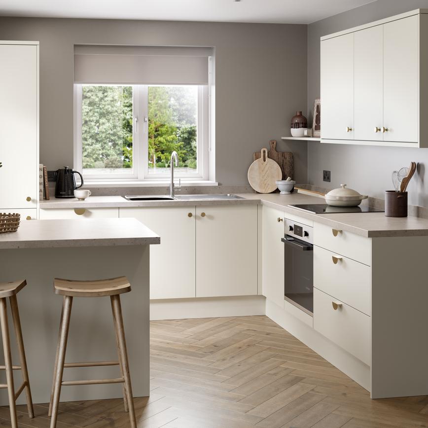 A warm white kitchen with slab doors in a peninsula layout. There are stone-effect worktops and herringbone oak flooring.