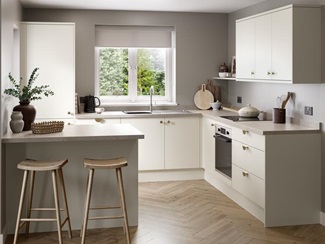 A warm white kitchen with slab doors in a peninsula layout. There are stone-effect worktops and herringbone oak flooring.