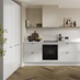 An l-shaped shaker kitchen, in a white colour. It has in-frame detailing with black handles and matching cabinet fixings.