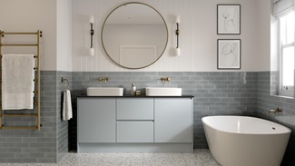 A bathroom in a pale, mist blue tone with large mirror. It has stone-effect flooring, 2-basing setup and brass tap fittings.
