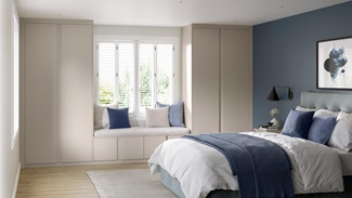 A bedroom with pale, sandstone door fronts. Between the wardrobes is a seated area, using matching storage as a bench.