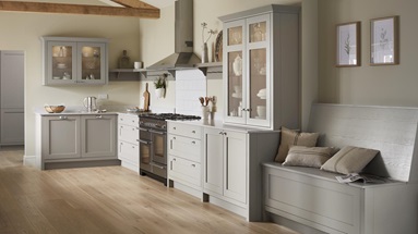 L shape kitchen in pebble grey with shaker style doors. Seated storage bench with cushions and worktop mounted glass cabinet.