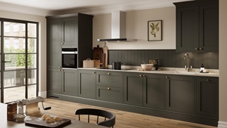 A dark-green kitchen with shaker doors in a single wall layout. Styled with brass handles, white worktops, and oak flooring.