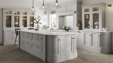 A stately kitchen featuring light-grey shaker doors with a beaded detail and glass dresser cabinets in an island layout.