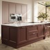 A two-tone, dark-red and light pink kitchen in an island layout. It has herringbone flooring and white worktops.