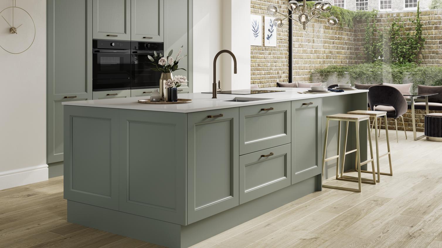 A reed green shaker kitchen in a single wall and island layout. There are black accessories, appliances, and wood floors.