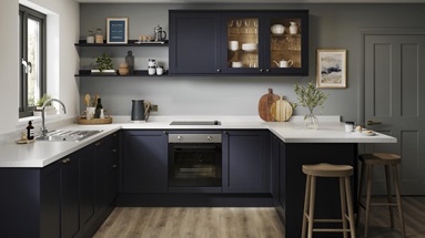 A U-shaped kitchen layout with navy, shaker doors. Includes white worktops, glass wall units, and a black, induction hob.