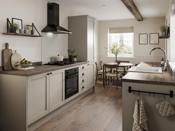 A rustic kitchen in a galley layout. Contains cream, shaker cupboards, dark-wood worktops, and a black, built-under oven.