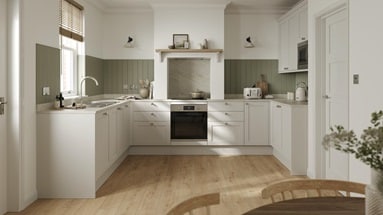 A porcelain coloured, shaker kitchen in a U-shaped layout. It has white worktops, green wall panelling, and plank flooring.