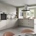 A sandstone kitchen design with matt slab doors, matt black knob handles and tap, and a stone-effect worktop and backboard