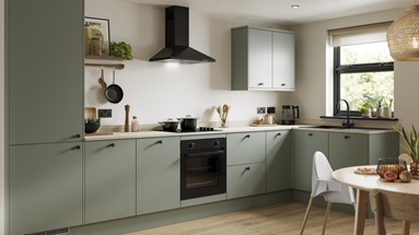 A modern green kitchen with cream worktops, black appliances and matching black accessories.