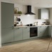 A modern green kitchen with cream worktops, black appliances and matching black accessories.