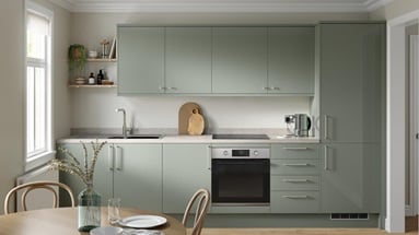 A gloss, reed green kitchen in a single wall layout. It has grey worktops, stainless steel sink, and integrated oven.