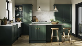 A fir green shaker kitchen idea in an island layout. Has white worktops, a ceramic sink, chevron flooring, and brass handles.