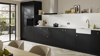 A one-wall kitchen with matt black cabinets and white worktops. Doors have brass handles and accessories.