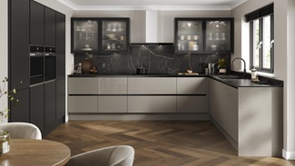 A handleless, l-shaped kitchen in a sand grey finish. There are fluted glass wall units and oak-style herringbone flooring.