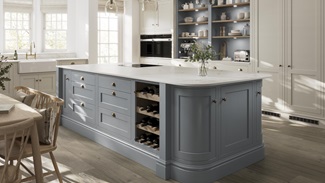 A blue shaker kitchen from Ilfracombe Dusk Blue, in an island layout with oak flooring. There is a run of linen-coloured cabinets