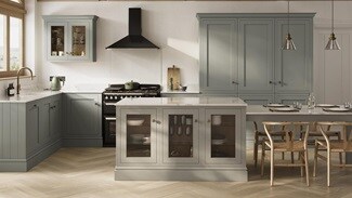 An Ilfracombe Estate Green shaker kitchen, in an l-shaped layout with island. It has oak flooring and metallic accessories.