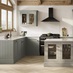 An Ilfracombe Estate Green shaker kitchen, in an l-shaped layout with island. It has oak flooring and metallic accessories.
