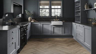 A dusk blue shaker kitchen idea in a u-shaped layout. Has cup handles, black worktops, chevron floors, and a Belfast sink.