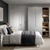 A matt dove grey bedroom with tall wardrobes and matching drawers. It has shelves in between and light, oak-style flooring.
